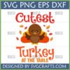 Cute Turkey Thanksgiving SVG design with 'Cutest Turkey At The Table' text and autumn leaves